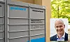 Postnord-pakkeautomat ved vegg med innfelt portrett av mann i dress til høyre