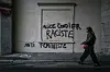 Person passerer vegg i Lyon med svart graffiti mot Alice Cordier og feminisme.