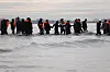 Gruppe migranter i oransje redningsvester går gjennom grunt vann mot en liten båt ved Gravelines.