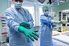 Kirurg og sykepleier iført munnbind tar på grønne operasjonshansker på operasjonsstue.