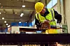 Fabrikkarbeider med hjelm kutter stål med vinkelsliper i en industrihall.
