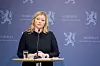 Kjersti Stenseng står ved talerstol med vannglass foran blå norsk regjeringsbakgrunn.