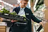 Butikkansatt setter ut friske grønnsaker i hyllen i en dagligvarebutikk.