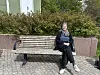 En person sitter avslappet på en benk i et utendørs område med busker og murstein. Hun heter Birgitte Lange.