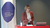Kvinne står ved en talerstasjon med laptop og banner for Institutt for samfunnsforskning.