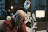 Eldre mann sitter bøyd med ansiktet i hendene mens en humanoid robot sitter ved siden av ham i en stue.
