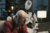 Eldre mann sitter bøyd med ansiktet i hendene mens en humanoid robot sitter ved siden av ham i en stue.