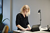 Blond kvinne jobber konsentrert ved laptop på et skrivebord i et lyst studio.