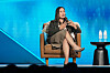 Daniela Amodei speaks on a stage with a blue backdrop beside a small table with water bottles.