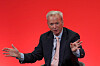 Eric Schmidt gestures while speaking onstage in front of a red background at a London investment summit.