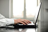 Nærbilde av en forretningsmann som skriver på laptop ved et vindu.