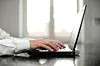 Nærbilde av en forretningsmann som skriver på laptop ved et vindu.