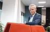 Hans Christian Holte står i et kontor, bak en stor oransje stol.