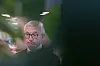 Karl Eirik Schjøtt-Pedersen taler innendørs, delvis skjult av uskarpe blader i forgrunnen.