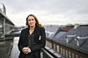 Arbeidstilsynets direktør Ingvill Kvernmo står ved et rekkverk på en takterrasse med urbant landskap i bakgrunnen.