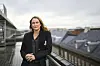 Arbeidstilsynets direktør Ingvill Kvernmo står ved et rekkverk på en takterrasse med urbant landskap i bakgrunnen.