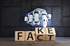 Hvit robotisk hånd flytter treklosser med ordene FACT og FAKE på et bord.