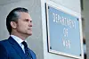 Defense Secretary Pete Hegseth stands beside a Department of War sign outside the Pentagon.