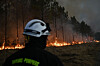 Brannmann i forgrunnen mens flammer brenner langs skogkanten.