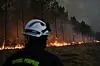 Brannmann i forgrunnen mens flammer brenner langs skogkanten.