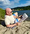 Jørund Rytman ligger på stranden og leser avis ved vannkanten.