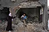 To personer står blant sammenraste betongrester foran en skadet bygning i al-Maghazi i Gaza.