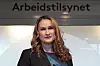 Ingvill Kvernmo står foran Arbeidstilsynets logo innendørs.