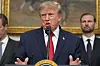 Donald Trump taler ved en talerstol, med to menn og et stort maleri i bakgrunnen.