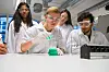 Videregåendeelever i verneutstyr utfører et kjemiforsøk rundt en laboratoriebenk.