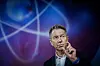 Terje Aasland gestikulerer foran en blå og lilla grafikk med atomlignende linjer.