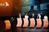 Panel med seks deltakere på en opplyst scene foran store skjermer og oransje podier.