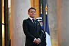 Emmanuel Macron står mellom søyler ved Élysée-palasset, med en vakt og franske flagg i bakgrunnen.