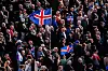 Folkemengde på rally i Reykjavik med flere islandske flagg hevet over menneskene.