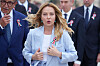 Giorgia Meloni i lyseblå jakke under en parade i Roma, omgitt av tjenestepersoner.