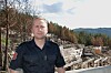 Kjetil Wetterstad Jensen, i uniform foran brannskadde bygningsrester med skog og ås i bakgrunnen.