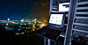 Bærbar datamaskin og serverrack med nettverksgrafikk over en opplyst by i Phuket om natten.