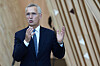 Jens Stoltenberg står i dress og snakker med hendene hevet foran en trevegg.