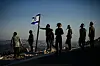 En gruppe mennesker står på en høyde ved solnedgang, med et israelsk flagg i vinden.