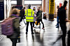 Streikevakt i gul refleksvest står i Oslo S mens reisende passerer.