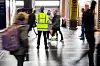 Streikevakt i gul refleksvest står i Oslo S mens reisende passerer.