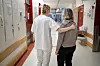 Sykepleier med armen rundt en pårørende kvinne i en lys sykehuskorridor.
