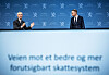 Eigil Knutsen og Jens Stoltenberg står foran en blå bakgrunn under overleveringen av skattekommisjonens rapport.