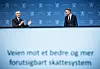 Eigil Knutsen og Jens Stoltenberg står foran en blå bakgrunn under overleveringen av skattekommisjonens rapport.