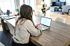 Person sitter ved et trebord og arbeider på en bærbar datamaskin i en lys bolig.