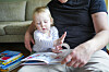 Barn og pappa leser en fargerik bok sammen i sofaen.
