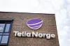 Telia Norge-logo på en teglsteinsbygning mot lys himmel.