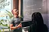 To programmerere diskuterer kode ved en bærbar datamaskin foran en stor skjerm på et lyst kontor.