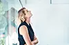 Blond forretningskvinne med korslagte armer ser opp i et lyst kontor.