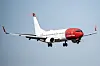 Norwegian-fly med rødt neseparti og utfelt landingsstell i luften mot blå himmel.