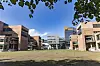 Åpent grøntareal omgitt av moderne bygninger på UiA-campus i Kristiansand under blå himmel.